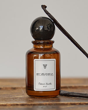 Raumduft Spray in kleiner, braunen Glasflasche mit schwarzem Deckel neben einer Vanillestange